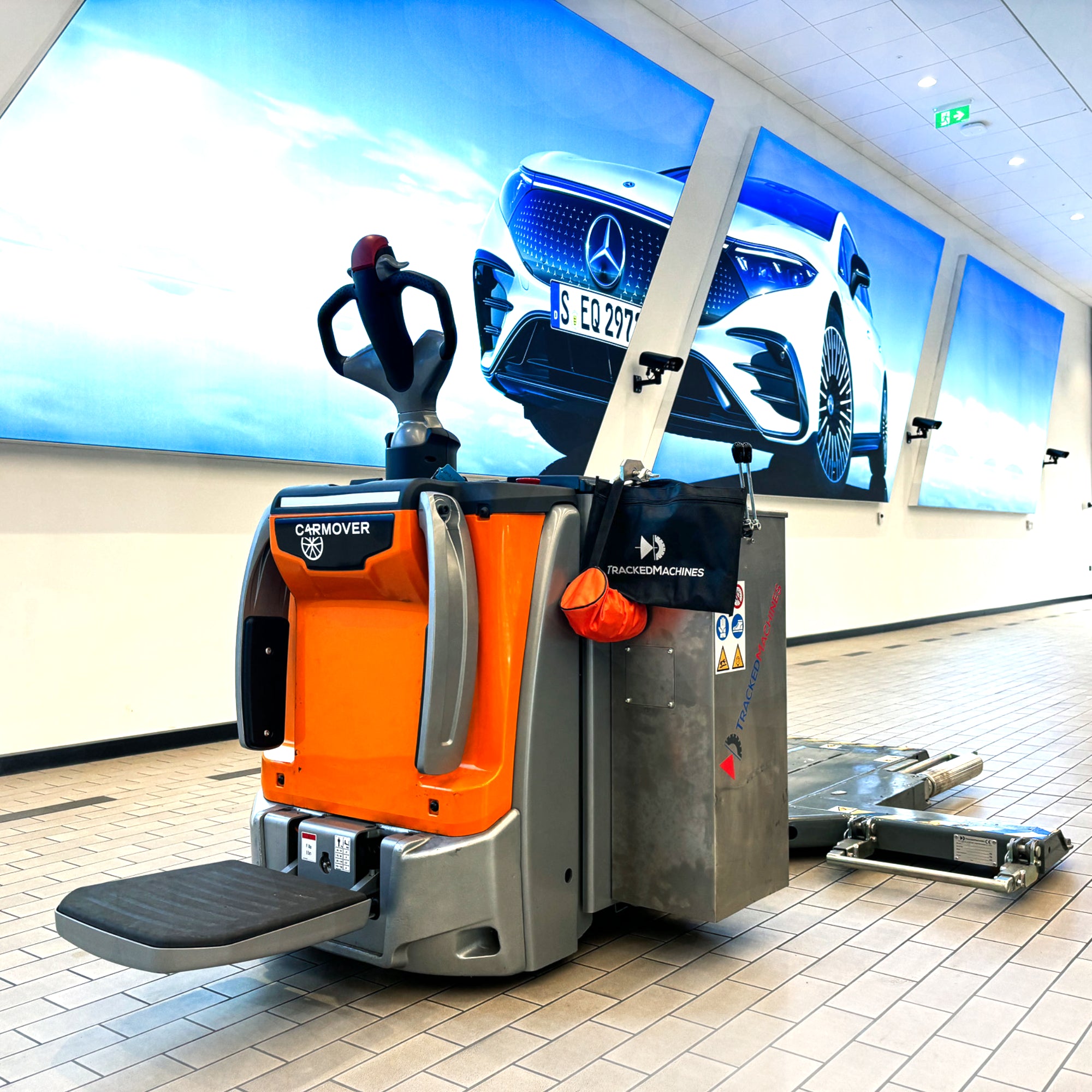 An orange and silver powered vehicle mover sat motionless in a car showroom